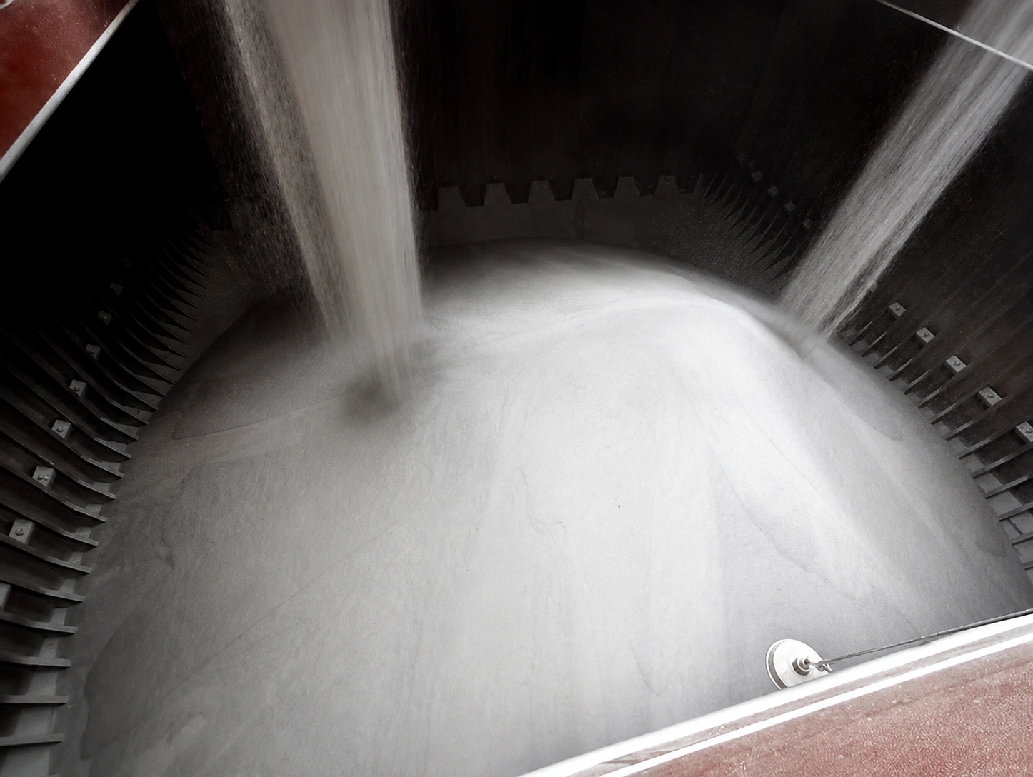 White granular cargo unloading through a chute into a vessel hold